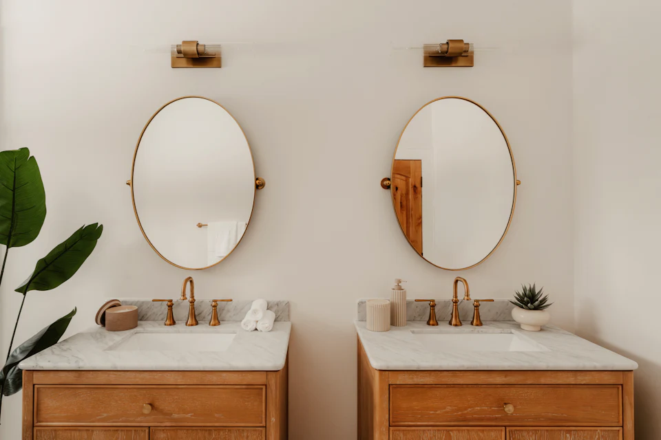 Double vanity with wood cabinets, oval mirrors and brass sconces