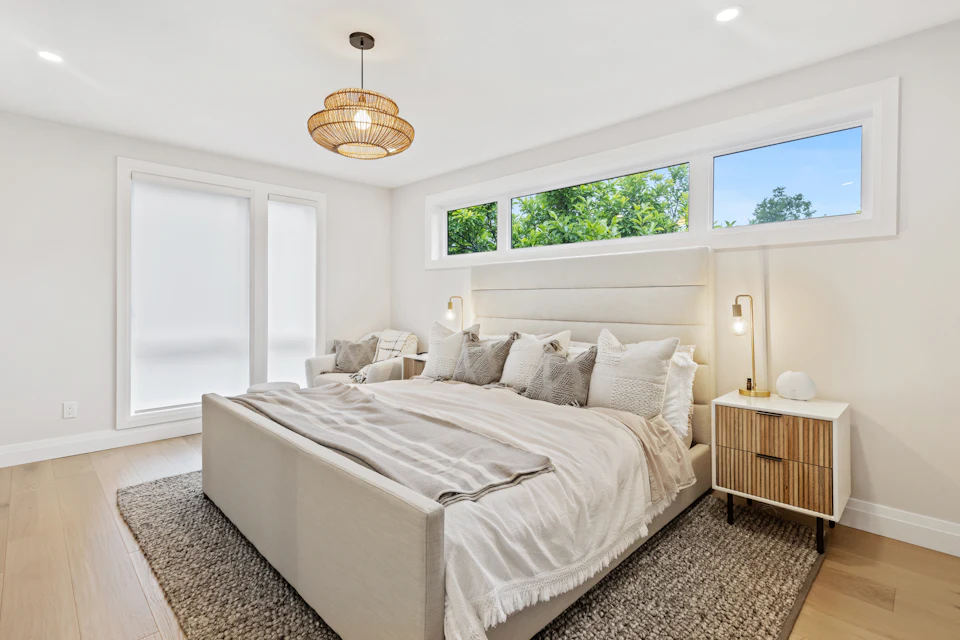 Bright primary bedroom staged with an upholstered bed, rattan pendant and woven rug