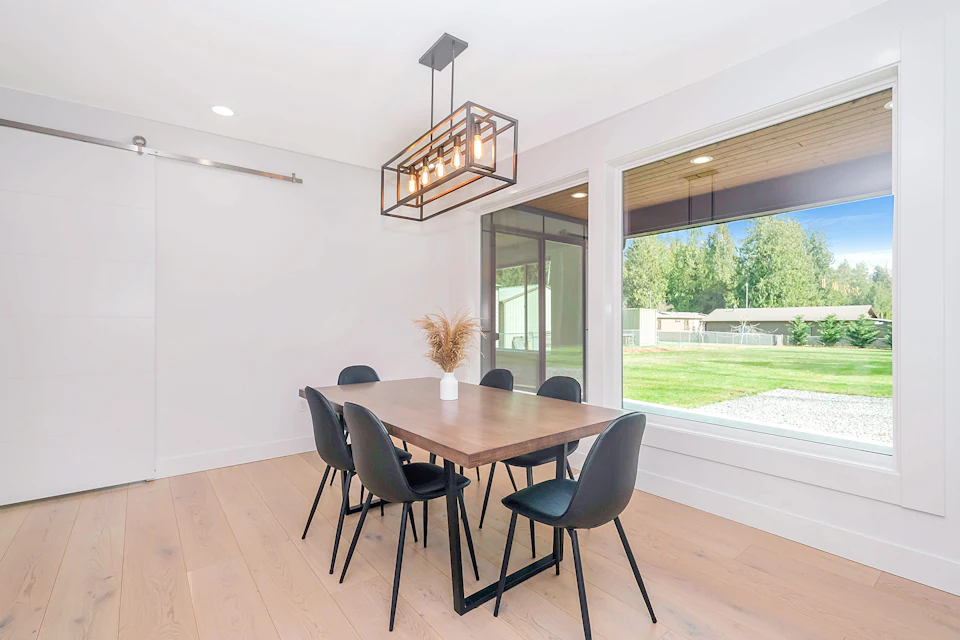 After staging — Dining area with a wood table, black chairs and a picture window to the garden