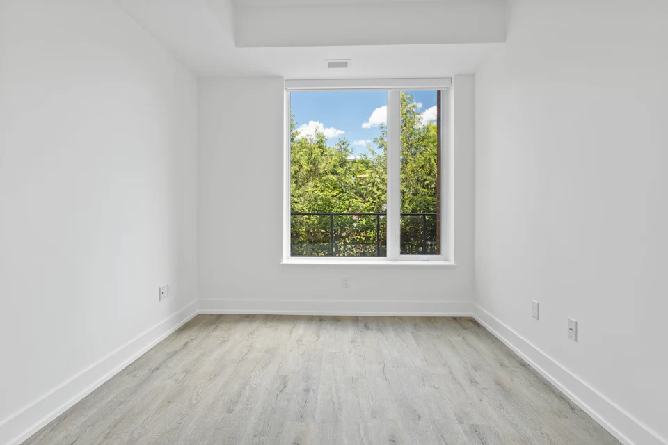 Before staging — Empty bedroom with a single window and pale wood floors