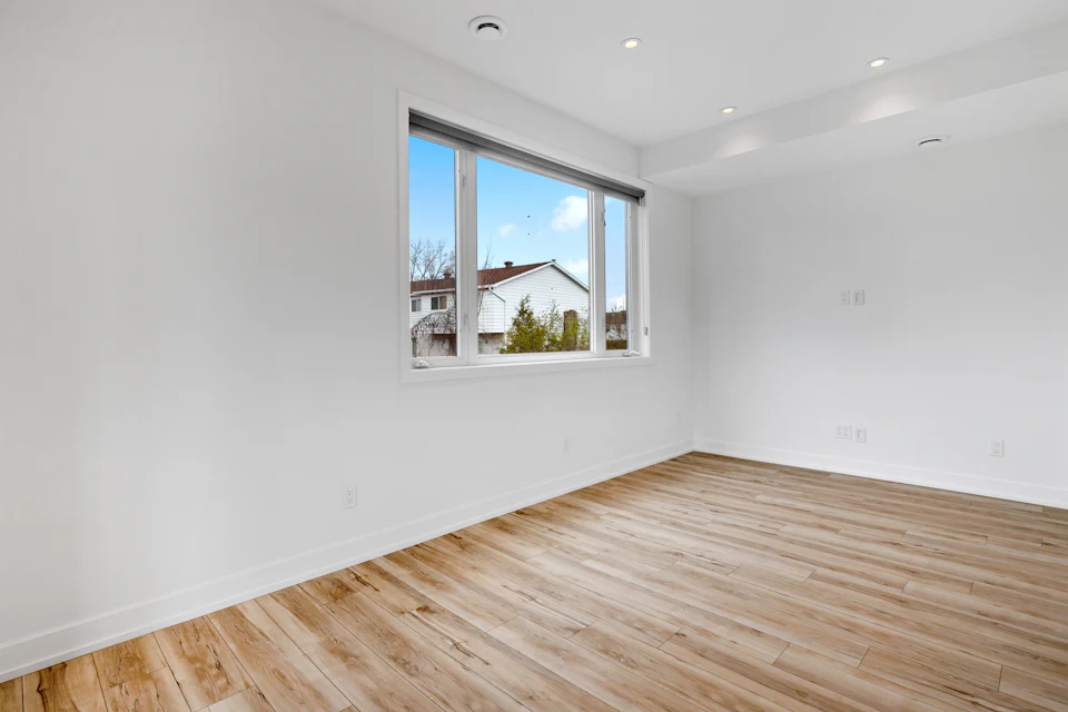 Before staging — Vacant room with oak floors and a wide window