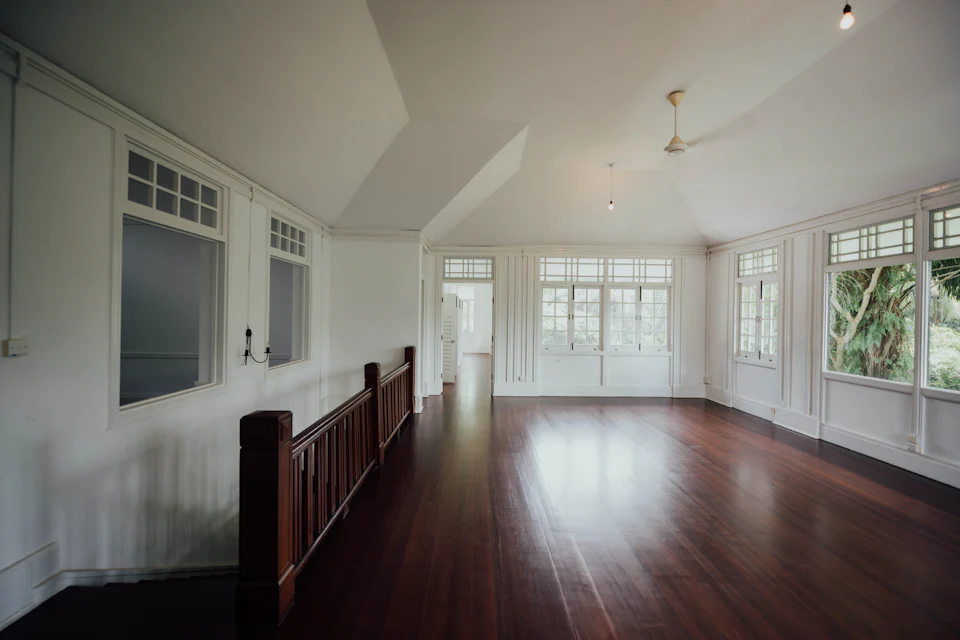 Before staging — Large vacant room with vaulted ceiling, dark wood floors and stair railing