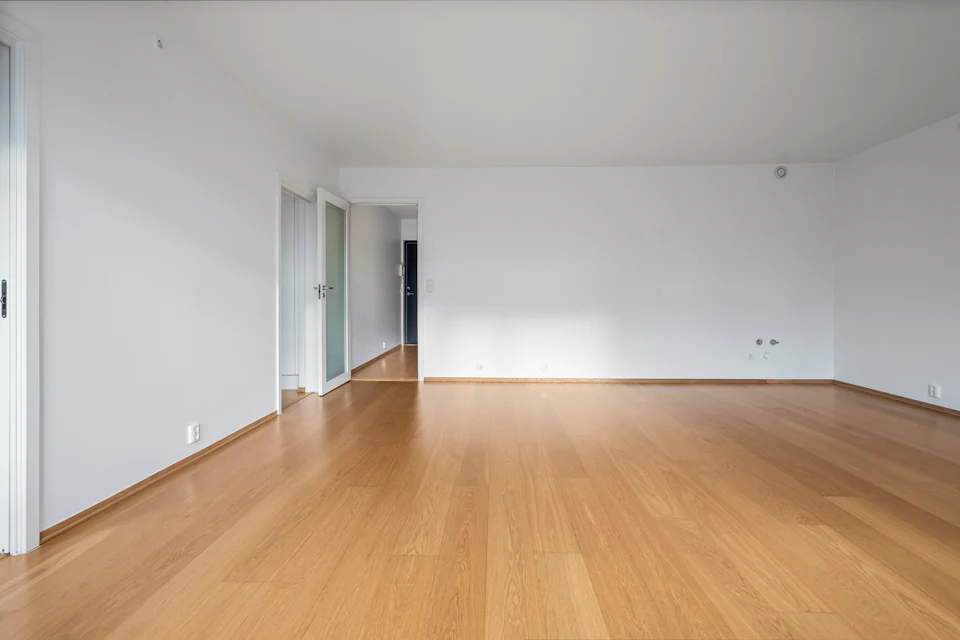Before staging — Wide empty living space with warm wood floors and white walls