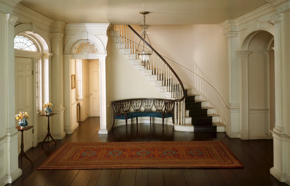 Traditional entry hall with a curved staircase, antique bench and Persian rug