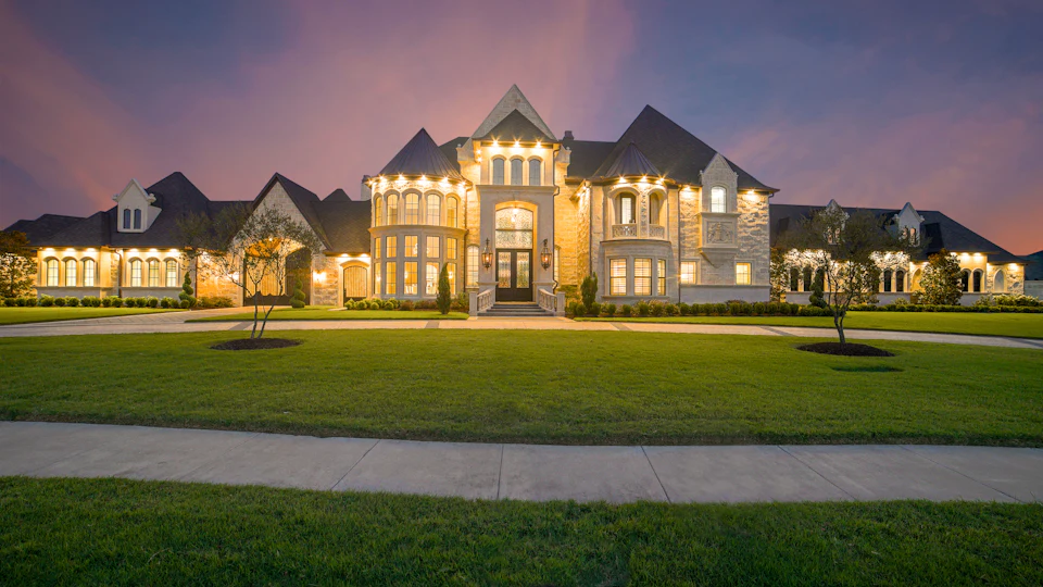 Grand luxury estate home glowing with warm exterior lighting at dusk