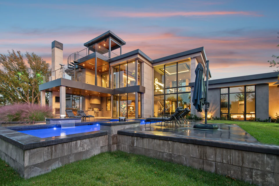 Contemporary luxury home with walls of glass and an illuminated pool at sunset