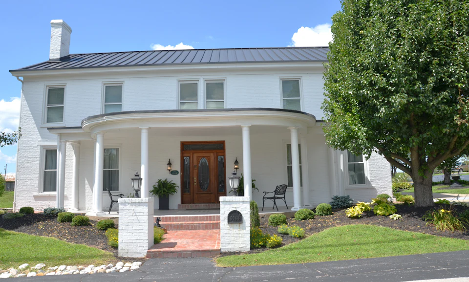 White Southern home with a columned front porch, metal roof and manicured lawn