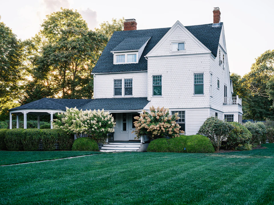 White Victorian-style home with a wraparound porch and blooming hydrangeas