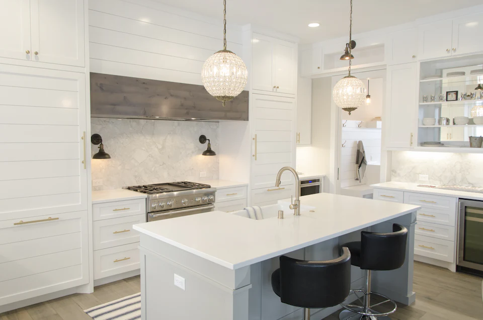 Transitional white kitchen with crystal pendants and an island with black stools