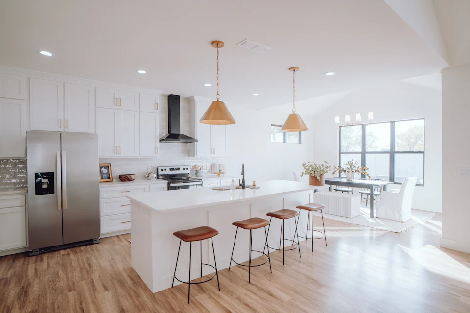 Open white kitchen with copper pendants, wood stools and a long island