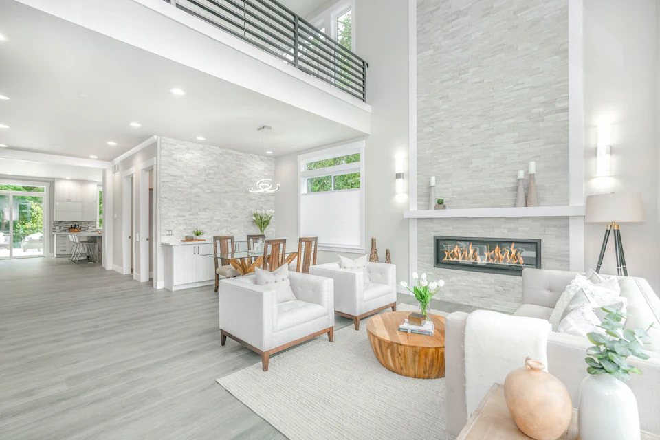 Two-story living room with a stone fireplace wall and white accent chairs
